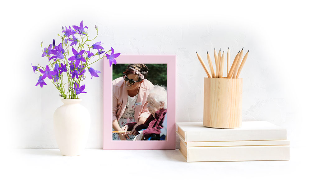 framed photo of Joanna and a patient, flanked by a white vase of purple flowers and a wooden cup oif pencils